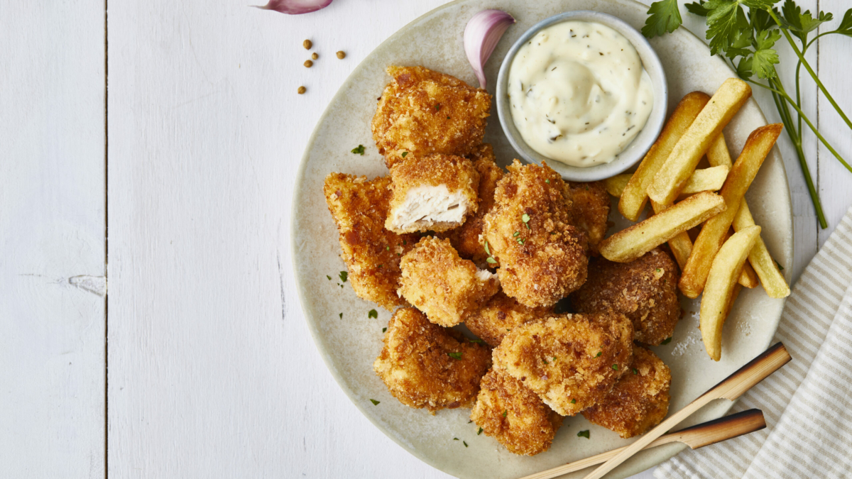 Chicken nuggets in a plate, with white sauce, garlic, french fries and lemon, served on a white wooden restaurant or home table, top view with copy space