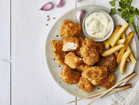 Chicken nuggets in a plate, with white sauce, garlic, french fries and lemon, served on a white wooden restaurant or home table, top view with copy space